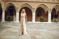 Beautiful lady in luxurious pink ballroom dress. Blond walking along the old castle. The blonde looks at the camera and travels