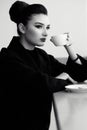 Beautiful lady with perfect make up and hair scrapped back into a high bun sitting at the bar and drinking coffee Royalty Free Stock Photo