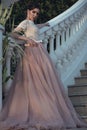 Beautiful lady with perfect make up in luxurious ballroom dress with tulle skirt and lacy top standing on stairs