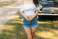 Beautiful lady standing near retro car.a girl in a white blouse and jeans shorts is holding a meadow flower, an elder, behind is a Royalty Free Stock Photo