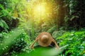 Beautiful lady in straw hat from back. Girl walks in the tropical jungle and looks at the sunset sun. Adventure, tourism,