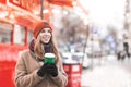 Beautiful lady wearing a cap and coat standing in the street with a cup of coffee in her hands, looking on copyspace and smiling. Royalty Free Stock Photo