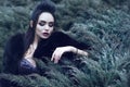 Beautiful lady wearing luxurious sequin dress and black sable fur coat sitting in coniferous bush and touching it with her fingers Royalty Free Stock Photo