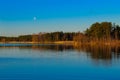 A beautiful lake in the forest, lit by the morning sun. The moon has not yet hidden Royalty Free Stock Photo