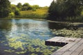 Beautiful landscape with calm water lake with wooden pier and yellow waterlilies, reeds, trees and forest Royalty Free Stock Photo