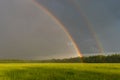 Beautiful landscape with a dramatic sky and a double rainbow. Green field under cloudy sky with double rainbow Royalty Free Stock Photo