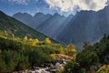 Beautiful landscape with high mountains with illuminated peaks, stones in mountain creek, blue sky