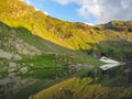 Beautiful landscape with high mountains with illuminated peaks, stones in mountain lake, reflection, blue sky and yellow sunlight Royalty Free Stock Photo