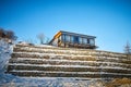 Beautiful landscape with a house on a cliff and a stone wall and fence in winter with snow and sun during sunset or Royalty Free Stock Photo