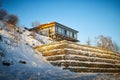 Beautiful landscape with a house on a cliff and a stone wall and fence in winter with snow and sun during sunset or Royalty Free Stock Photo