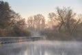 Beautiful landscape image of sunrise mist on urban lake with sun beams streaming through tress lighting up water surface Royalty Free Stock Photo