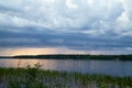 Beautiful landscape with lake, sky and clouds, rain and sunset on the horizon on background and green glass on foreground Royalty Free Stock Photo