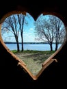 Beautiful landscape of water, green coast with trees and blue sky visible through heart shaped hole in wooden door Royalty Free Stock Photo