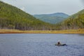 A fisherman on a rubber boat with oars floats on a calm lake amid green hills Royalty Free Stock Photo