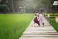 Beautiful Lao woman sitting alone with decorate flower on wooden bridge in green rice field