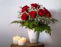 Beautiful bouquet of red roses in a vase and two lighted candles on a small table on a white background Royalty Free Stock Photo