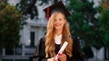 Beautiful with a large smile lady graduate posing in front of the camera while holding her diploma in the college garden