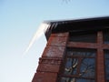 Beautiful large transparent icicle illuminated by the sun hangs from the roof of the house