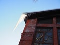 Beautiful large transparent icicle illuminated by the sun hangs from the roof of the house