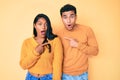 Beautiful latin young couple wearing casual clothes together surprised pointing with finger to the side, open mouth amazed Royalty Free Stock Photo