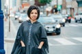 Beautiful Latin young woman in grey stylish poncho with fringe in urban street. Fashion and street style. Pretty hispanic brunette