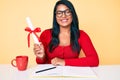 Beautiful latin young woman with long hair holding graduate degree diploma looking positive and happy standing and smiling with a Royalty Free Stock Photo