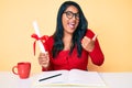 Beautiful latin young woman with long hair holding graduate degree diploma pointing thumb up to the side smiling happy with open Royalty Free Stock Photo