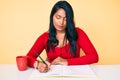 Beautiful latin young woman with long hair writing a book sitting on the table thinking attitude and sober expression looking self Royalty Free Stock Photo