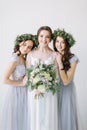 Beautiful laughing bride in a white wedding dress holding bouquet with bridesmaids in blue grey dresses and wreathes