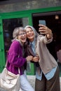 Beautiful laughing mature Asian lady with companion take selfie with smartphone on city street Royalty Free Stock Photo