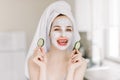 Beautiful laughing young woman with hair wrapped in bath towel, with facial mask on her face holding slices of fresh Royalty Free Stock Photo