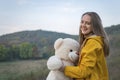 Beautiful laughing young woman with teddy bear on autumn day. Happy young woman in yellow parka jacket walks in nature Royalty Free Stock Photo