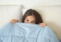 Beautiful lazy young woman lying down in the bed and sleeping. Teen girl with open eyes covers her face with blanket in the mornin