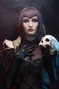 A beautiful leggy busty cosplay girl wearing an erotic leather costume poses holding fake human skull in her hands on a dark