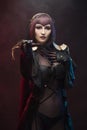 A beautiful leggy busty cosplay girl wearing an erotic leather costume poses and makes gestures with her hands on a dark Royalty Free Stock Photo