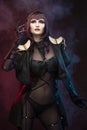 A beautiful leggy busty cosplay girl wearing an erotic leather costume poses and makes gestures with her hands on a dark Royalty Free Stock Photo