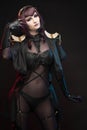 A beautiful leggy busty cosplay girl wearing an erotic leather costume poses and makes gestures with her hands on a dark Royalty Free Stock Photo