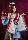 Beautiful leggy busty cosplayer girl wearing a stylized Japanese kimono costume cheerfully posing holding a fake pipe on a blue