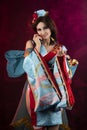 Beautiful leggy busty cosplayer girl wearing a stylized Japanese kimono costume cheerfully posing holding a fake pipe on a blue