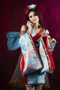 Beautiful leggy busty cosplayer girl wearing a stylized Japanese kimono costume cheerfully posing holding a fake pipe on a blue