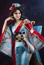 Beautiful leggy busty cosplayer girl wearing a stylized Japanese kimono costume cheerfully posing holding a fake pipe on a blue