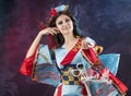 Beautiful leggy busty cosplayer girl wearing a stylized Japanese kimono costume cheerfully posing holding a fake pipe in the wind