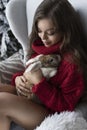 Beautiful leggy young girl, wearing red sweater and wool socks sits at the window and gently holds a rabbit in her hands in