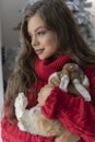 Beautiful leggy young girl, wearing red sweater and wool socks stays at the window and gently holds a rabbit in her hands in