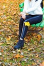 Beautiful legs girl in black pants and boots with yellow leaves in the hands of sitting on the bench in autumn Park Royalty Free Stock Photo