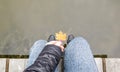 Beautiful legs of a girl in jeans are sitting on a wooden bridge by the lake, holding a yellow maple leaf in their hands. Autumn Royalty Free Stock Photo