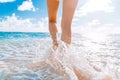 Beautiful legs of a young girl who runs towards the ocean on a sandy beach. The wave breaks against the girl`s legs. Ghostly ocea Royalty Free Stock Photo