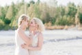 Beautiful lesbian couple walking on sand along river bank on their wedding day