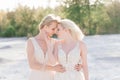 Beautiful lesbian couple walking on sand along river bank on their wedding day