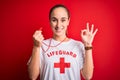 Beautiful lifeguard woman wearing t-shirt with red cross using whistle over isolated background doing ok sign with fingers,